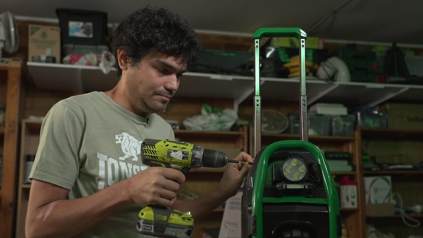 A man using a drill on an electronic device in a shed