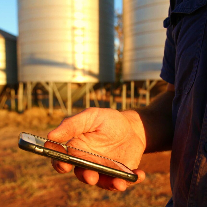 A man stands with a phone in his hand by a silo