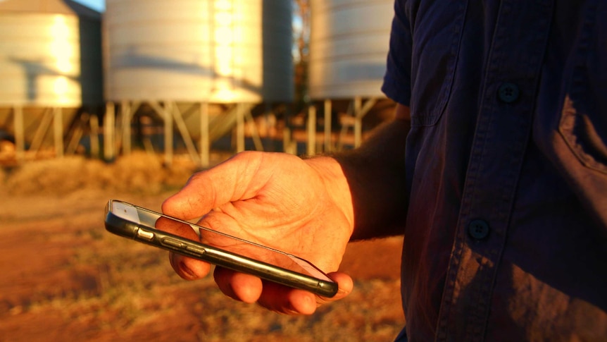 A man stands with a phone in his hand by a silo