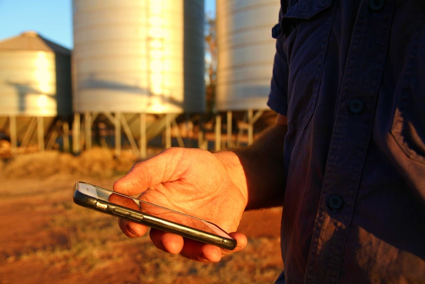 A man stands near a silo with a phone in his hand.