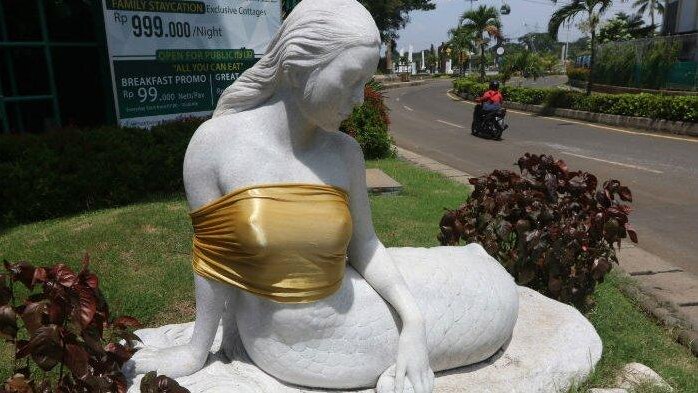 A statue of a mermaid sitting down with her breast covered in gold cloth.