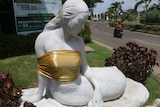 A statue of a mermaid sitting down with her breast covered in gold cloth.