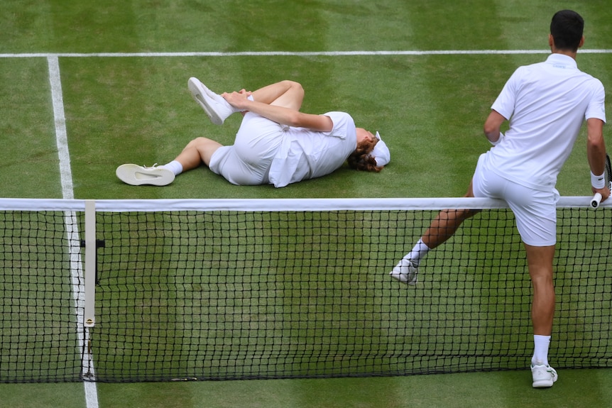Novak Djokovic walks over the net to check on a fallen Jannik Sinner