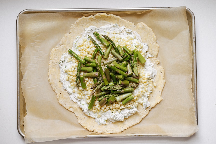 Pastry topped with spring onion cream cheese, corn kernels, asparagus, to be formed into a vegetarian galette.