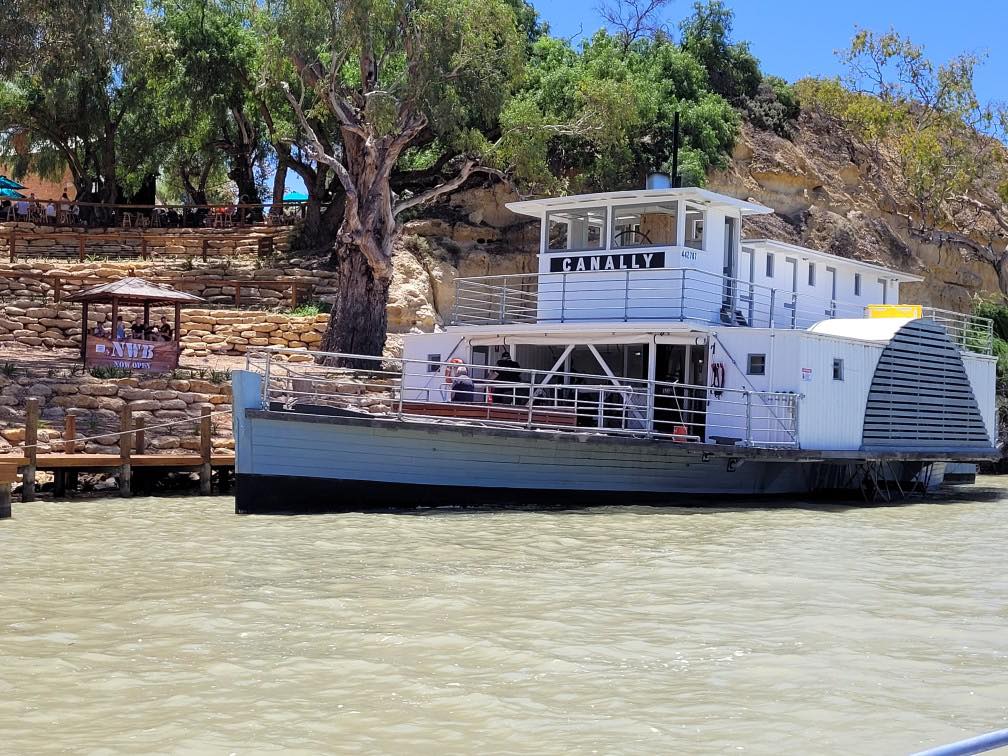 Un gran barco de vapor blanco con la palabra Canally escrita. Detrás de ellos hay acantilados y caminos rocosos.