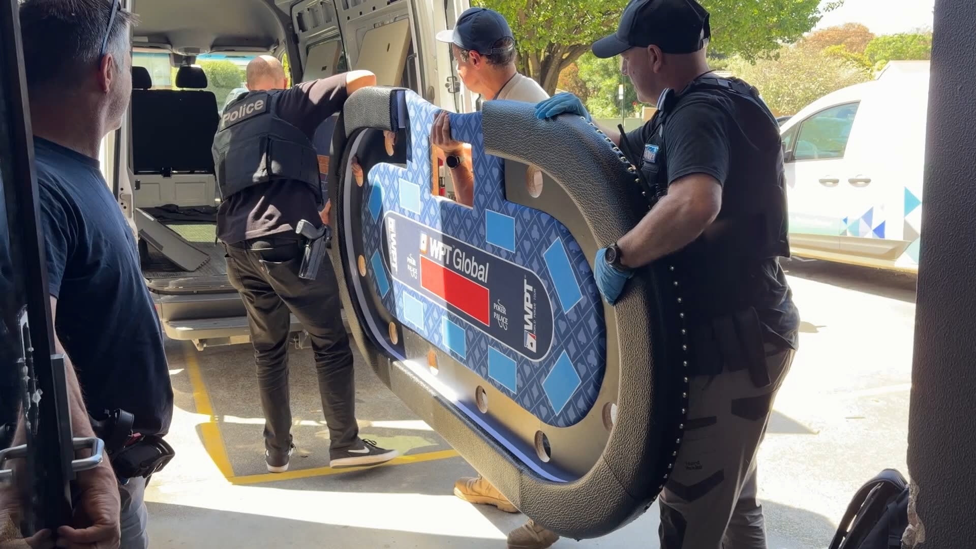 Three police officers load a casino table into the back of a van.