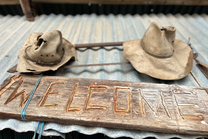 A welcome sign on a corrugated iron shed, with two battered Akubra-style hats above it.