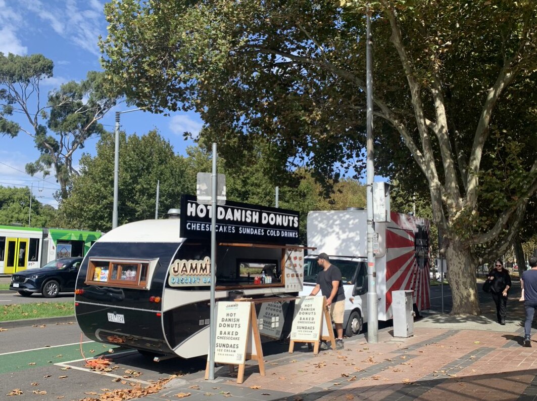 A man sets up his danish doughnut food truck at the side of the street.