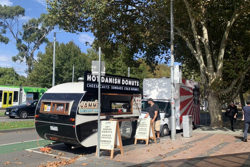A man sets up his danish doughnut food truck at the side of the street.