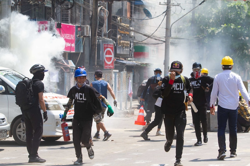 Masked men run in different directions in a city street filled with teargas.