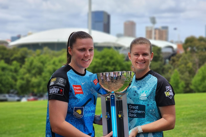 Two women hold a trophy with Adelaide Oval in the background