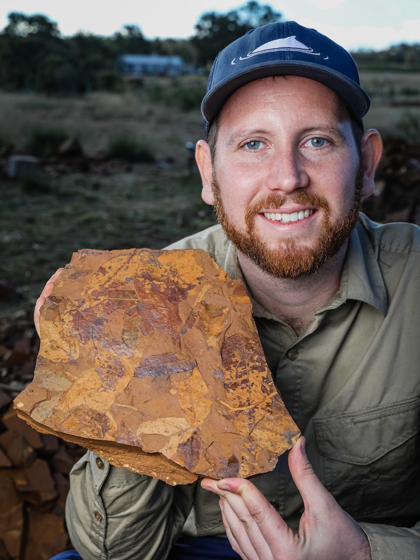 Dr Matthew McCurry, with a red beard, holds up a rock containing ancient fossils 