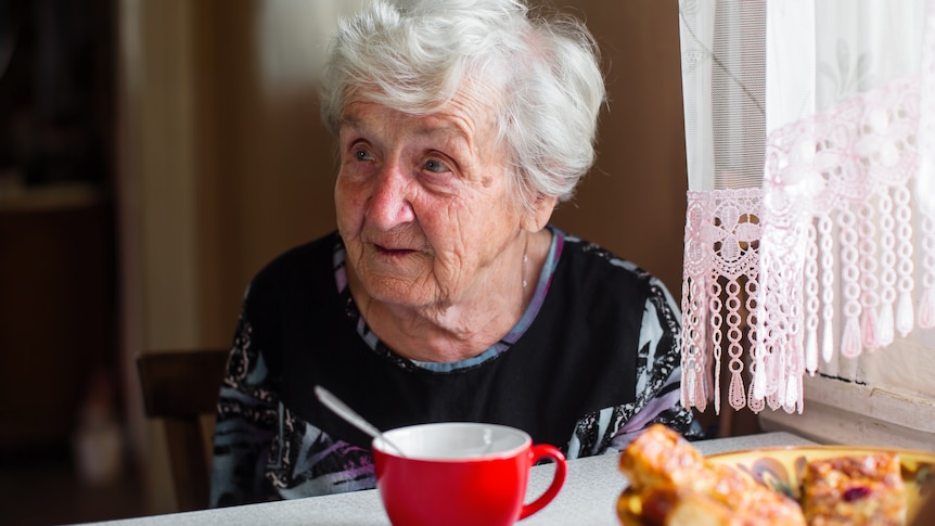 Older lady sits at kitchen table with a mug in front of her