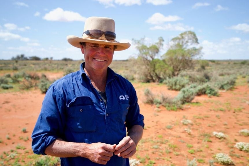 A man in a blue shirt and hat smiles in the Australian outback.