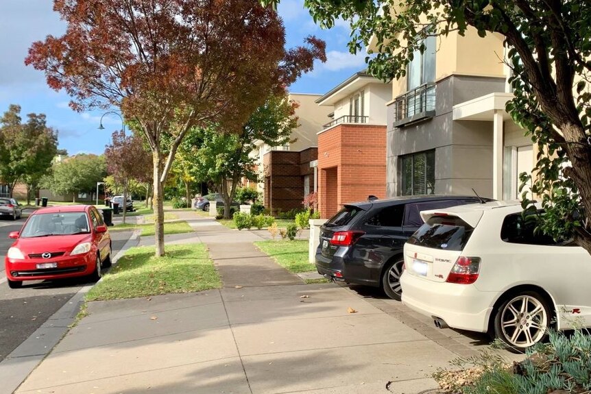 A row of new townhouses with cars parked in the driveways and on the street.