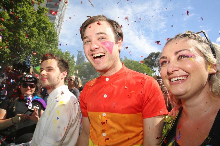 Three millennials look thrilled as red confetti flies in the sky in Melbourne.