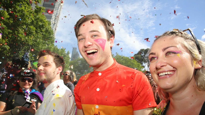 Three millennials look thrilled as red confetti flies in the sky in Melbourne.