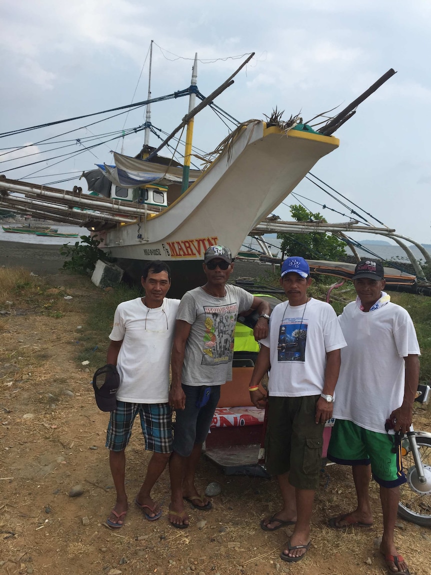 Filipino fishermen stand in front of their fishing boat.