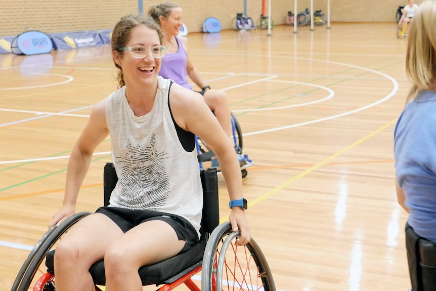A woman in a wheelchair on a basketball court smiles .