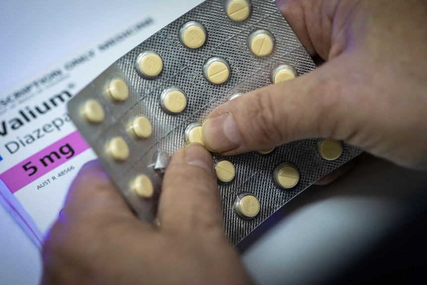 A close up of fingers pushing a small yellow tablet out of its blister pack