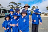 Seven children in school uniform in a courtyard.