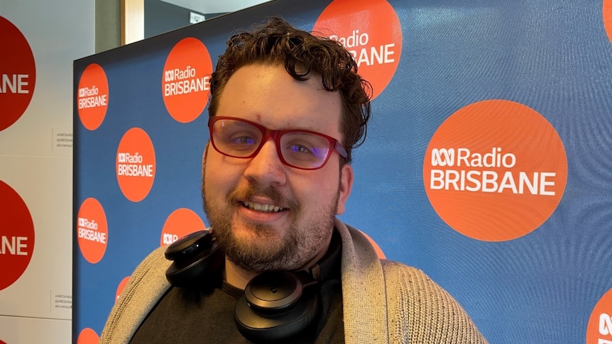 Oliver Hetherington-Page smiles in front of an ABC Radio Brisbane wall.