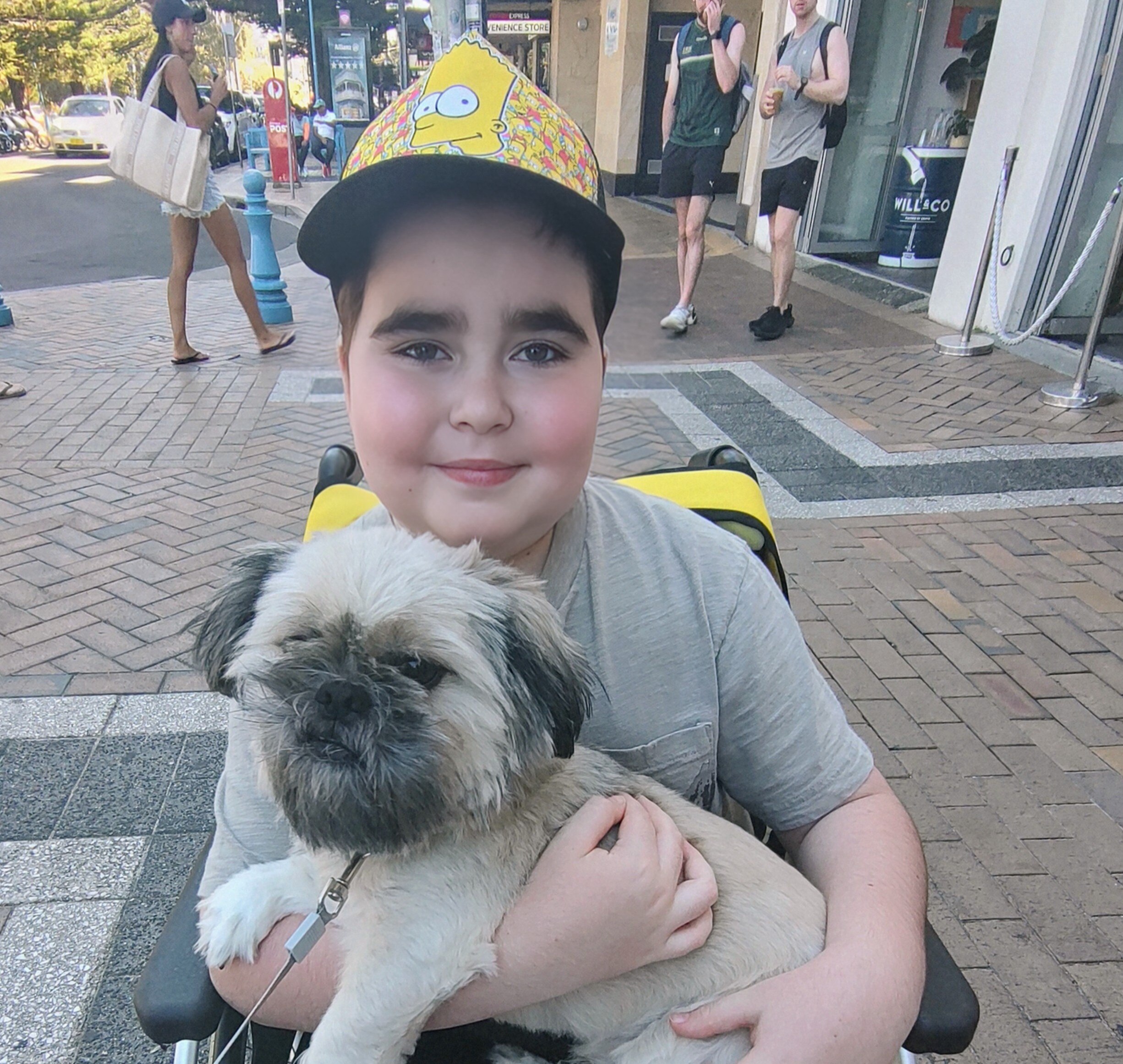 Um jovem de boné sentado em uma cadeira de rodas segurando um cachorro terrier branco.