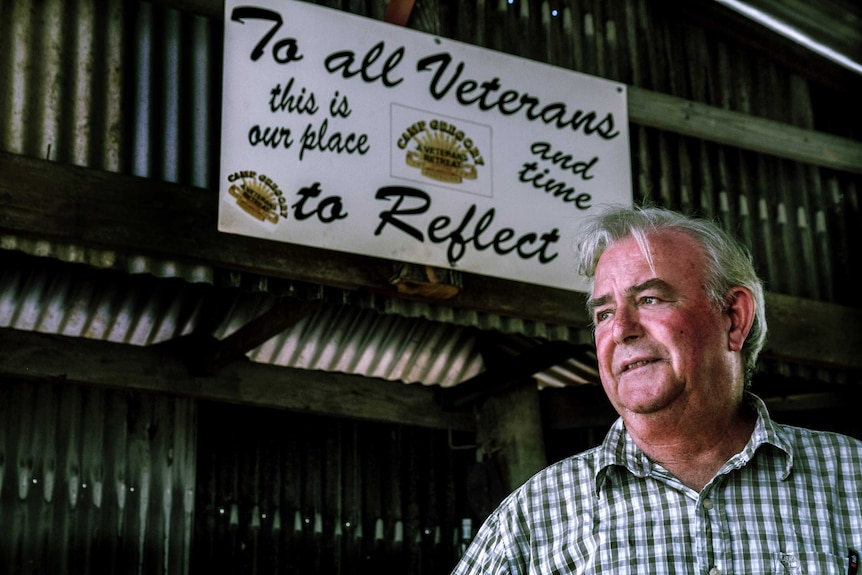 A man stands below in a shed, below a welcome sign for veterans