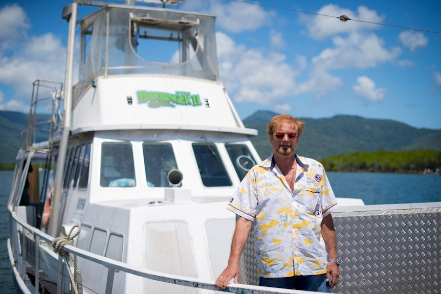 A man stands on the bow of a white boat holding on to the handrail.