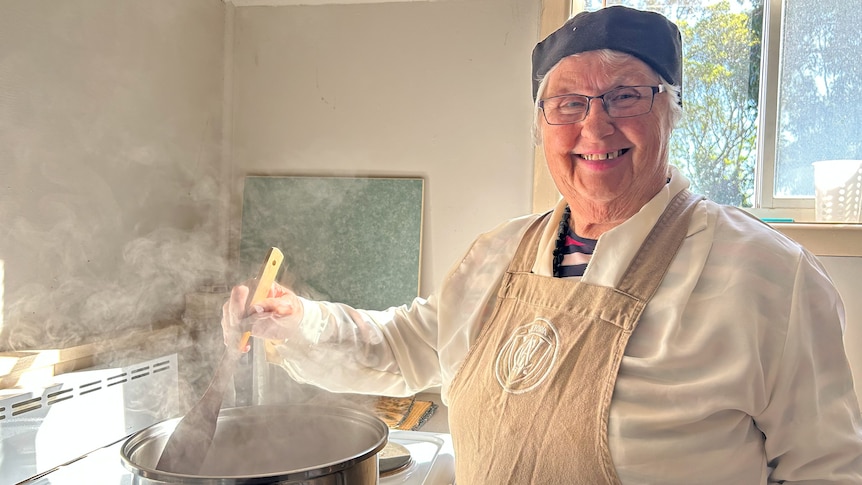 Mary Grant stands over the stove, stirring a pot of jam while wearing her CWA apron.