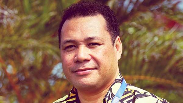 A Fijian Samoan man with short dark hair and features amongst palm trees outside wearing an island bula shirt