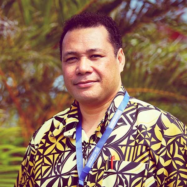 A Fijian Samoan man with short dark hair and features amongst palm trees outside wearing an island bula shirt