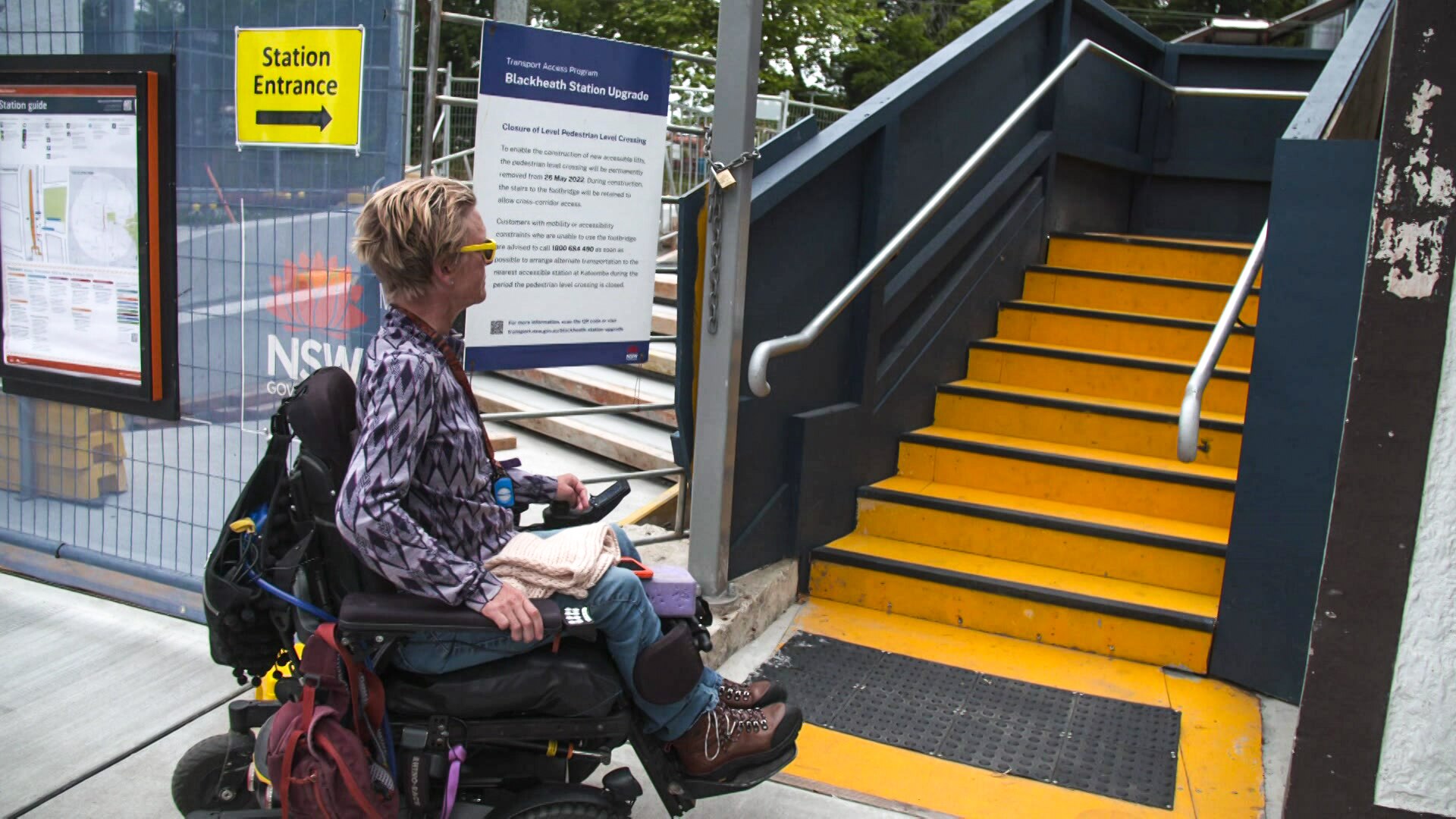Woman in a wheelchair looks up at a set of concrete stairs at a train station