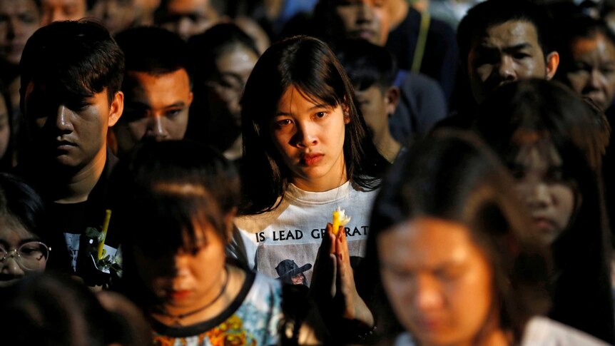 A woman stares at the camera from a crowd of people with bowed heads.