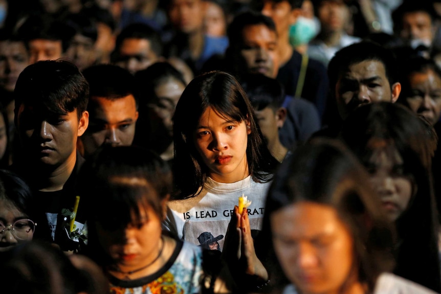 A woman stares at the camera from a crowd of people with bowed heads.