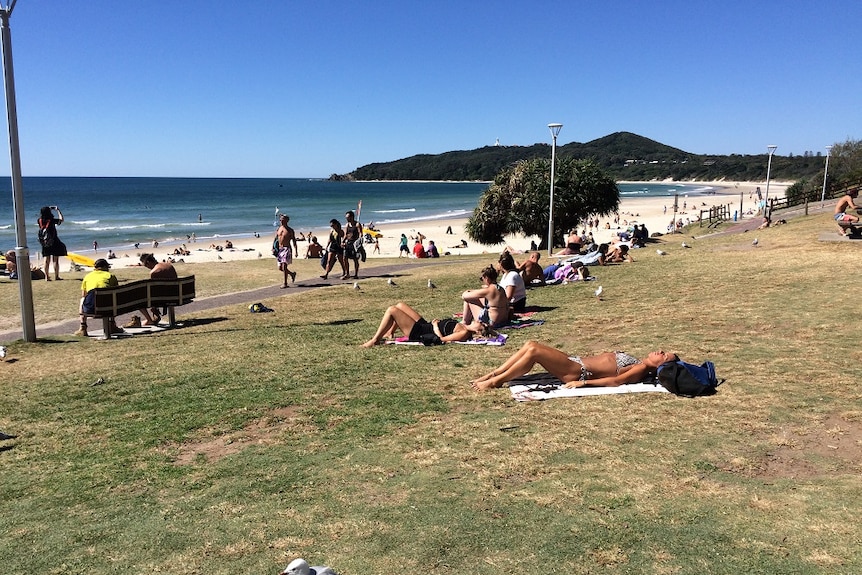 People on the Byron Bay beachfront with iconic lighthouse in the background
