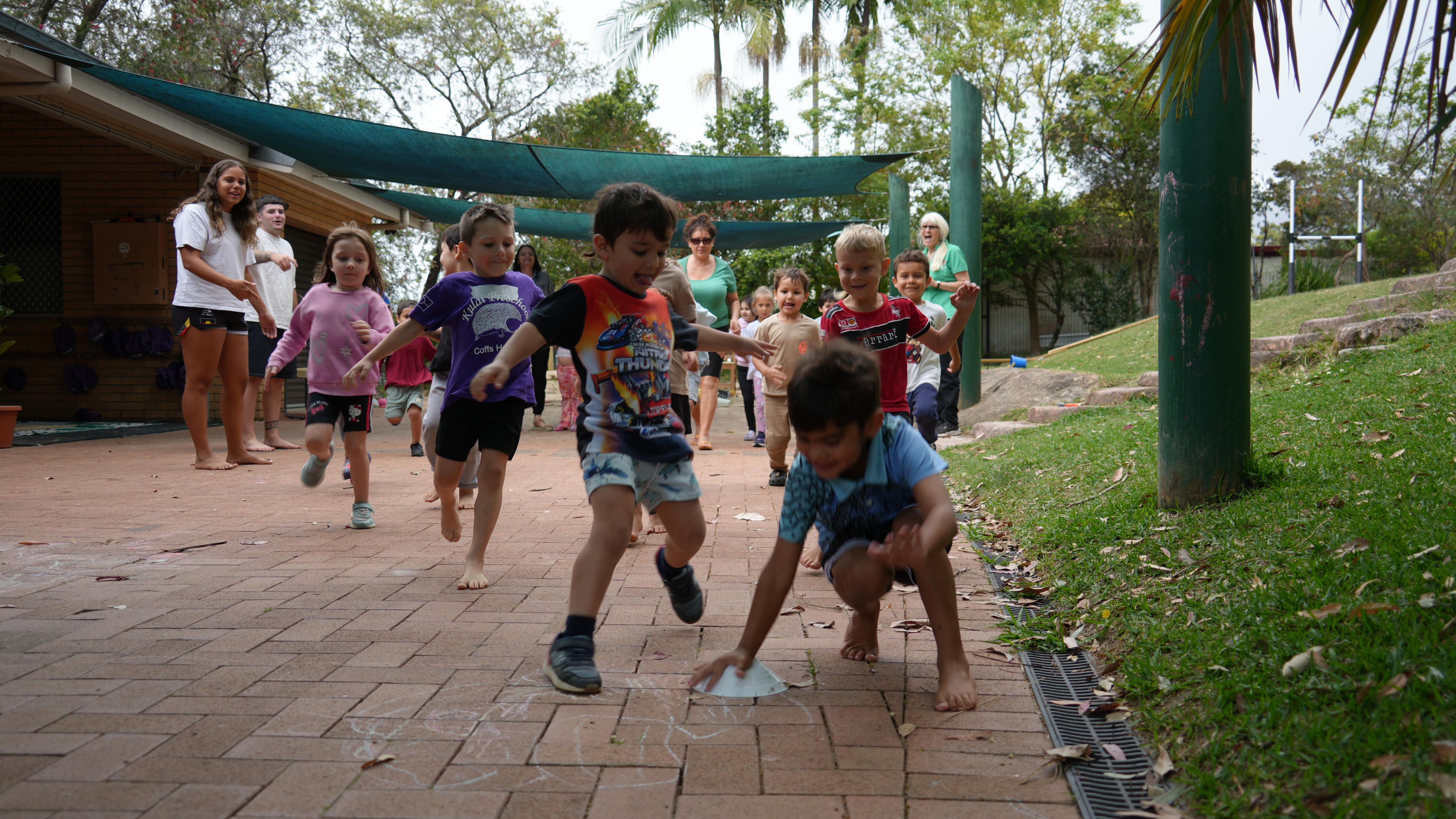 Little kids running toward a cone touching it on a paved area of a preschool garden