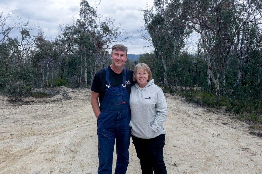 A couple stand in the centre of a dirt road surrounded by gum trees