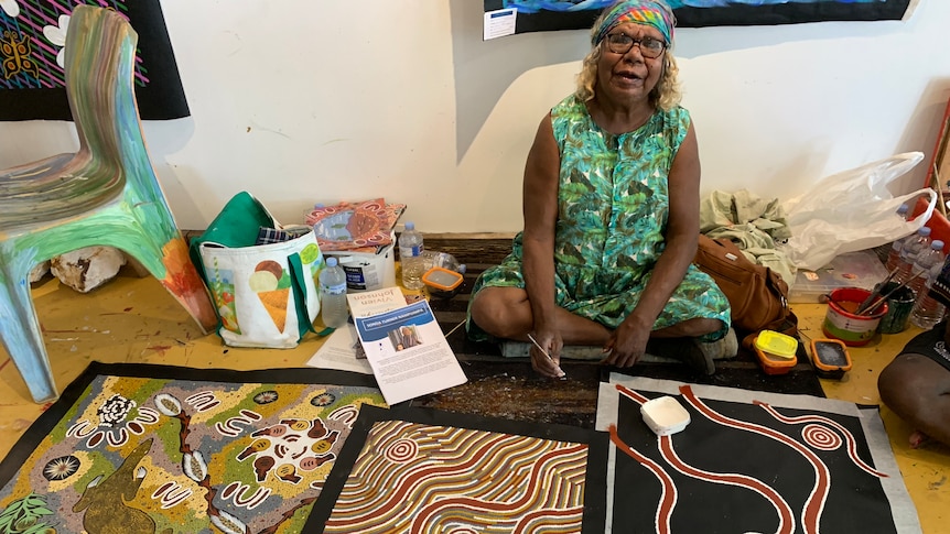 A woman sitting next to her paintings.