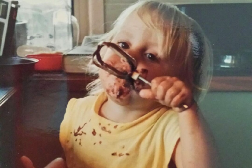 Old photo of a young boy licking chocolate cake mixture off a beater.