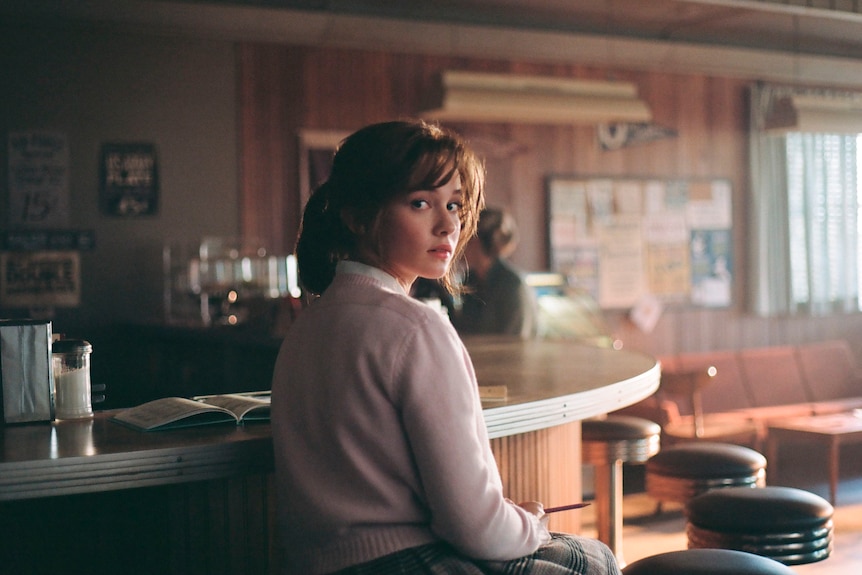 Cailee Spaeny sitting on a diner stool while in character as a teenager Priscilla Presley. 