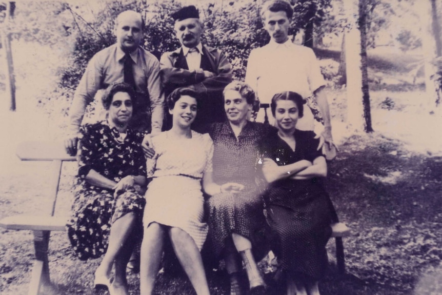 Seven people pose for a photograph. It is an old black and white photo and they are dressed in Russian attire.