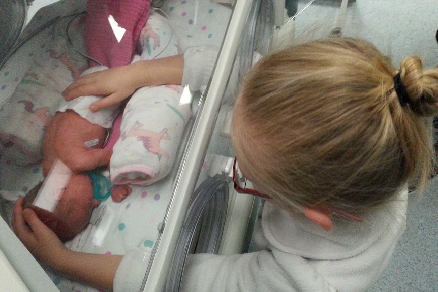 A little girl gently touches her prematurely born sister in a humidicrib.