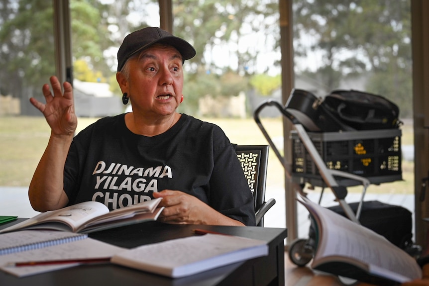 Woman wearing a cap and Djinama Yilaga choir t-shirt sit at table deep in conversation.