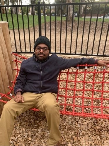 A man sits on a piece of equipment in a playground. 