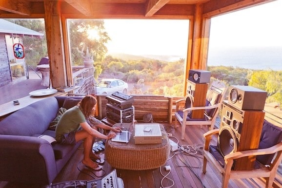 A man sits on a couch playing with recording equipment in a farm house near the sea.