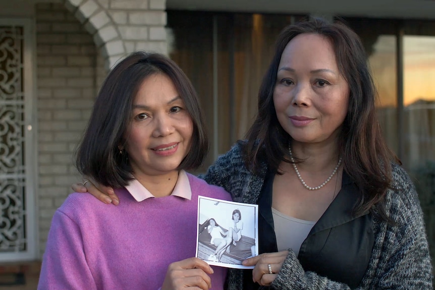 Two Vietnamese women hold a black and white photograph of themselves as girls aboard a navy ship