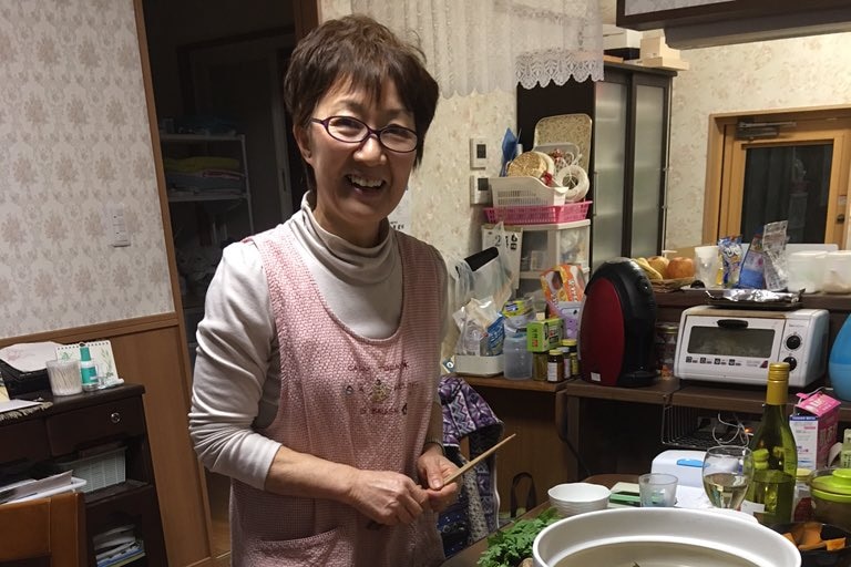 Japanese woman in her kitchen next to hot pot and sliced meat and vegetables, at Rikuzentakata