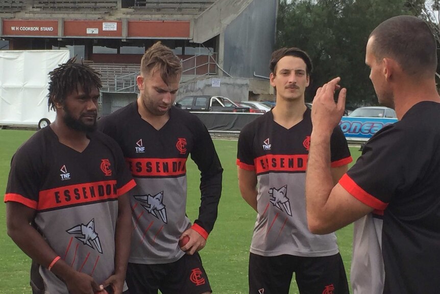 Patrick Matautaava stands next to two players while a coach addresses them.