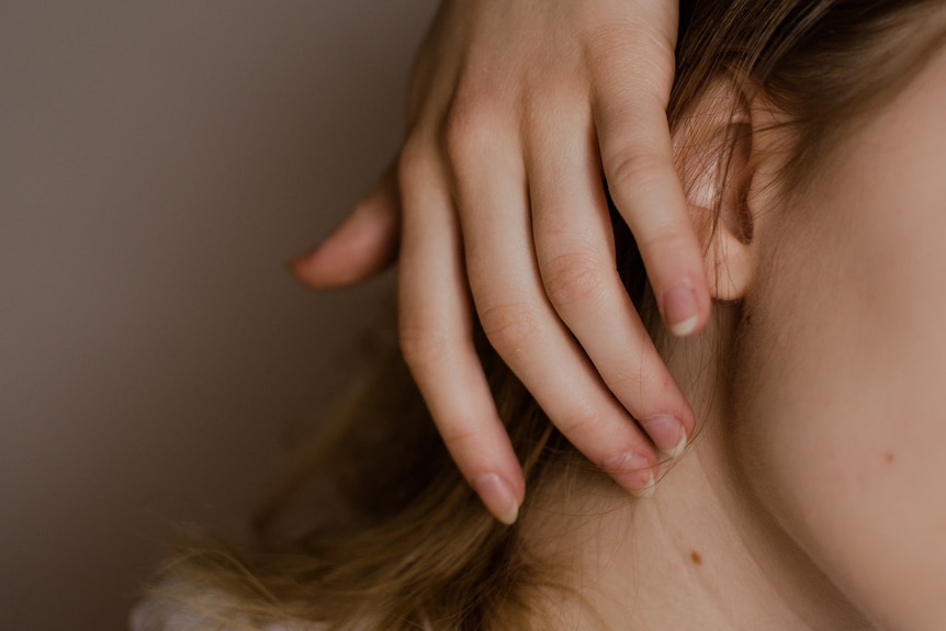 A woman pushes back her hair to expose a mole on her neck